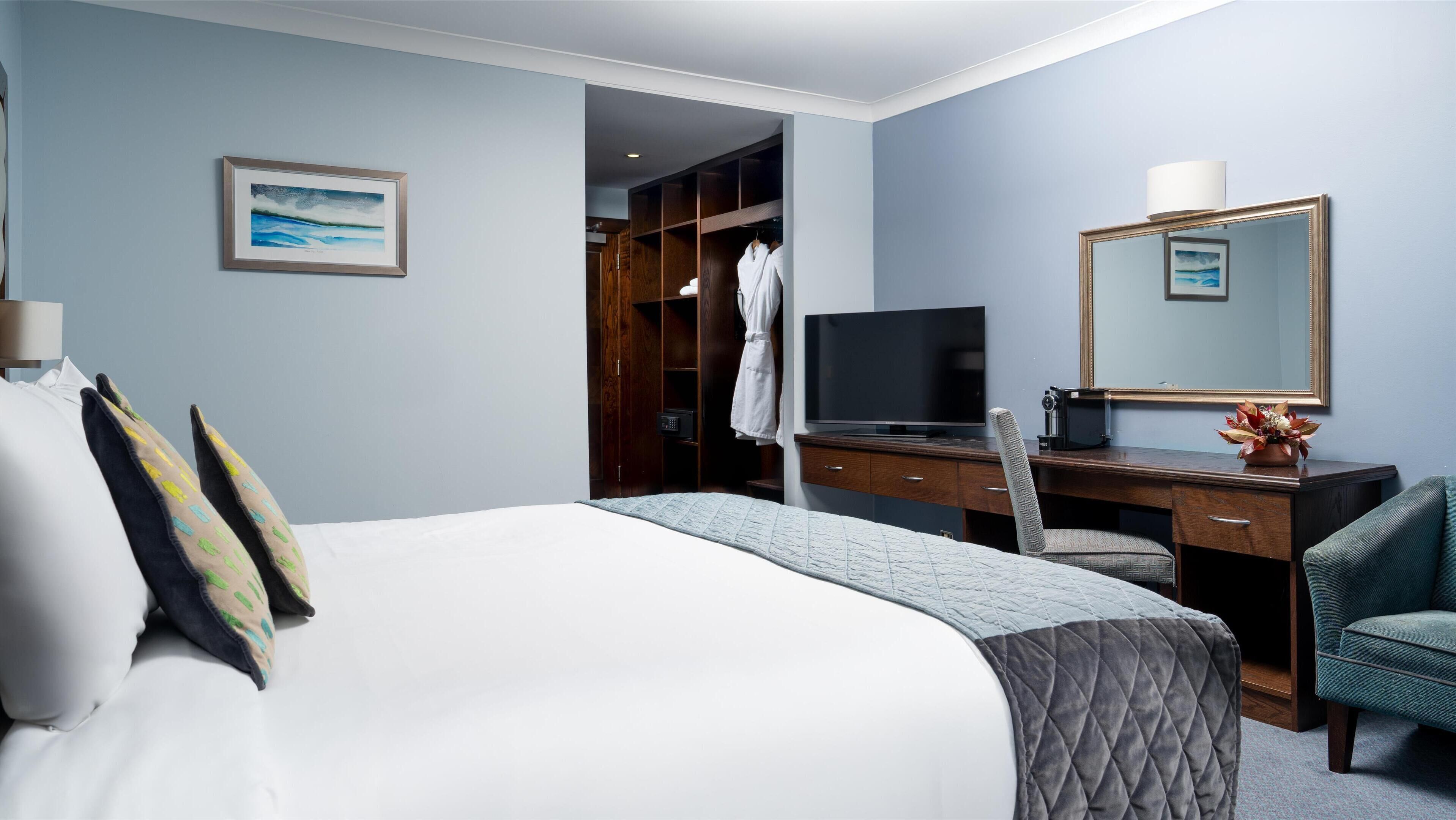 A hotel room with a bed, a desk with a TV, a mirror, and a wardrobe.