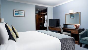 A hotel room with a bed, a desk with a TV, a mirror, and a wardrobe.
