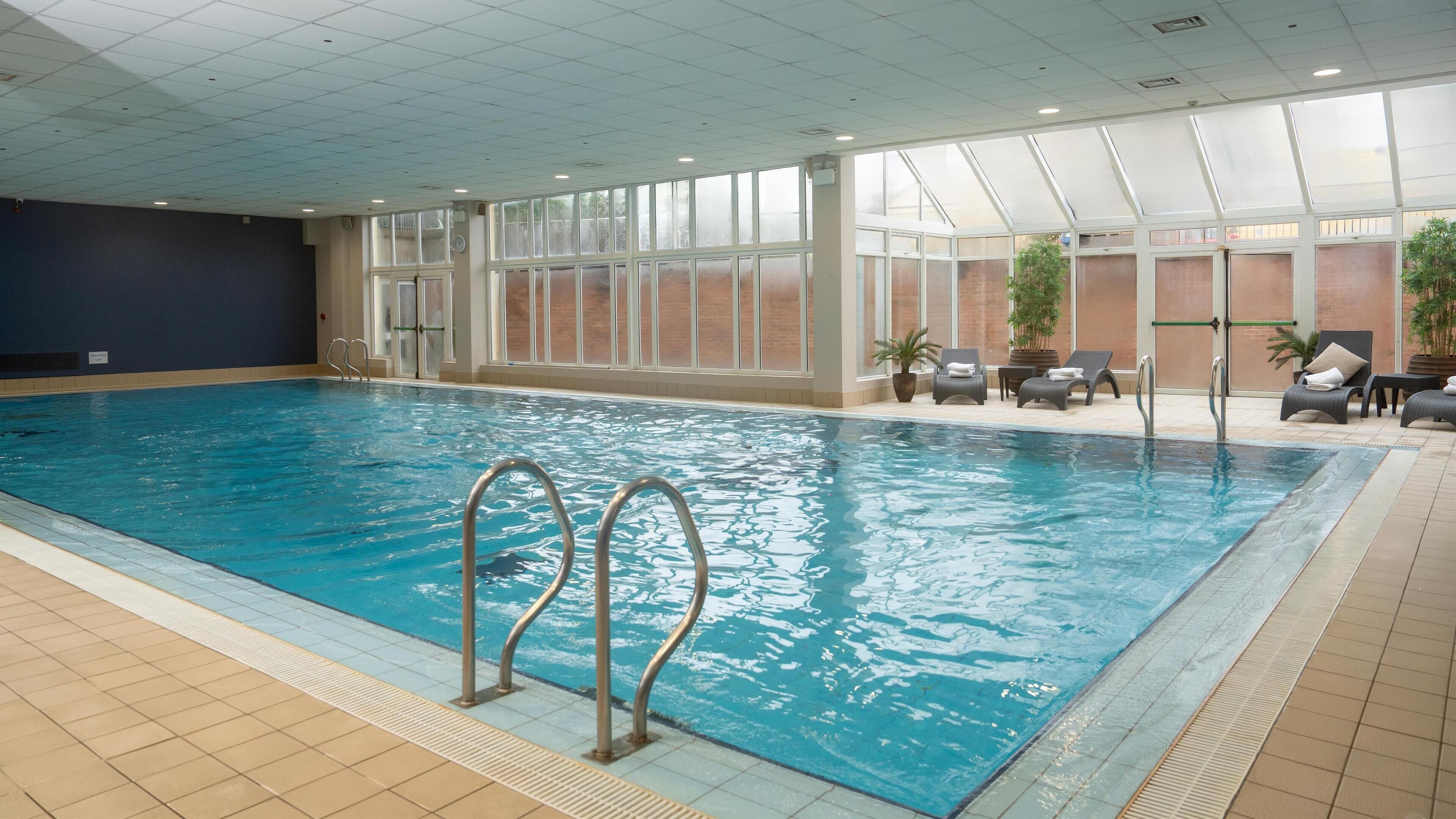 An indoor swimming pool with clear water, surrounded by lounge chairs and potted plants.