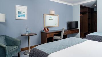Hotelkamer met twee bedden, een bureau met een televisie, een stoel, een tafeltje met een fles en glazen, en een ingelijste foto aan de muur.