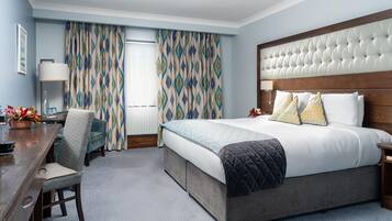 Habitación de hotel con una cama grande, cabecero de madera, escritorio con silla y cortinas estampadas.