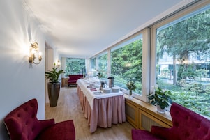 Un comedor con una mesa larga dispuesta para una comida, ventanas amplias con vistas a la vegetación y sillas tapizadas en rojo.