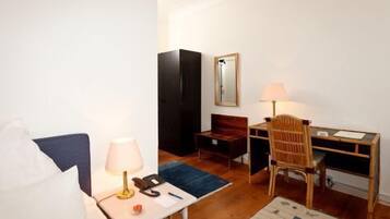 Une chambre d’hôtel de taille réduite, comprenant un lit, un bureau, une chaise, une lampe, une armoire et un miroir.