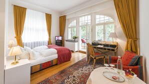 A hotel room with a bed, a desk, a chair, a table with a tray, and a television. - Parkhotel Atlantic Heidelberg (Heidelberg)