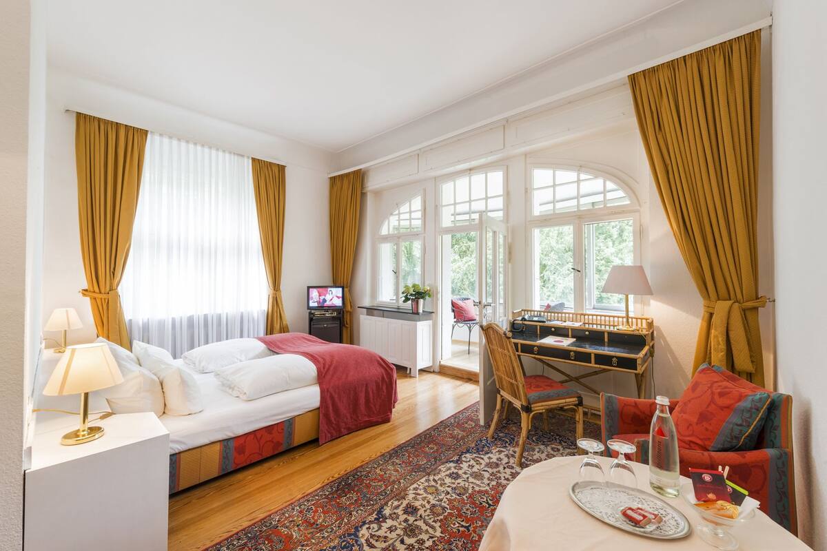 A hotel room with a bed, a desk, a chair, a table with a tray, and a television.