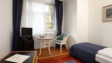 Una habitación pequeña con cama, televisor, silla, mesa y ventana con cortinas.