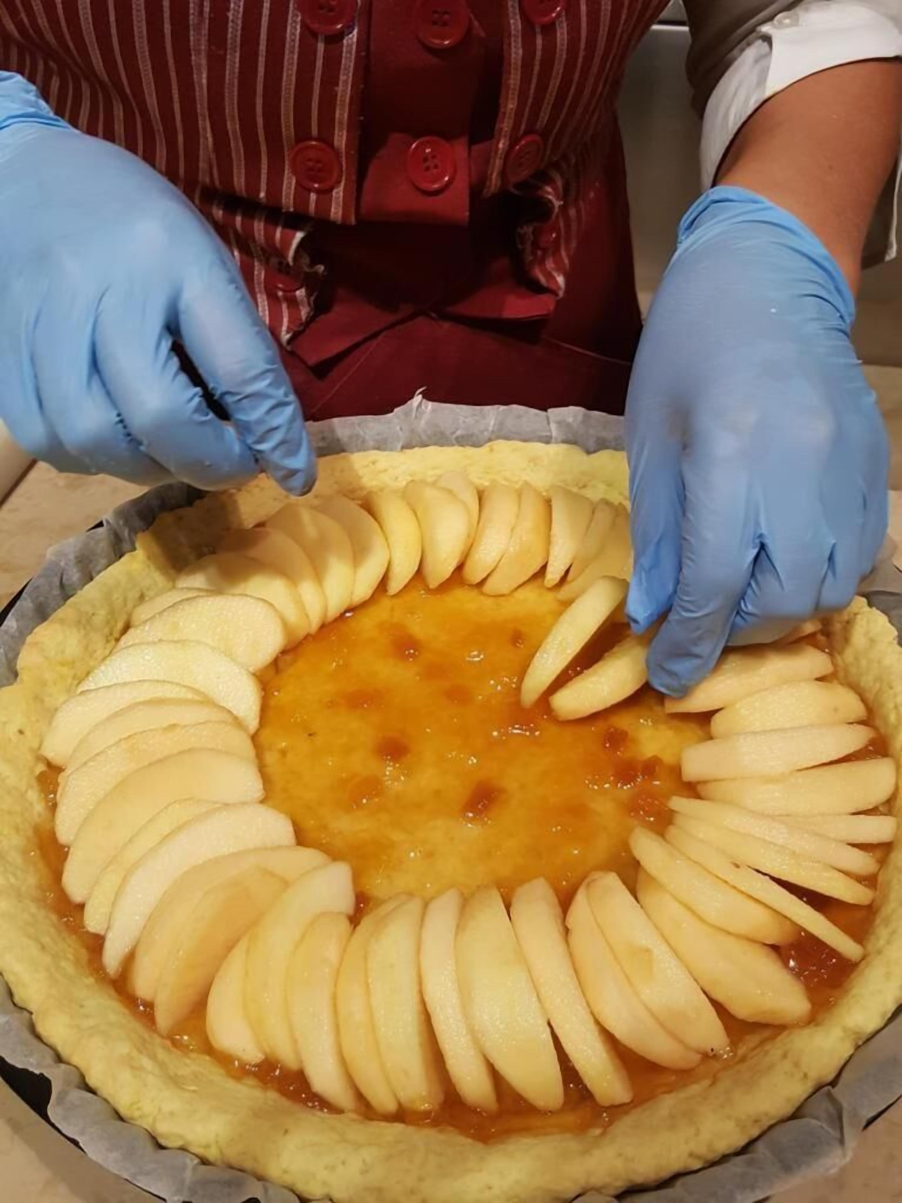 A person placing apple slices in a tart crust.