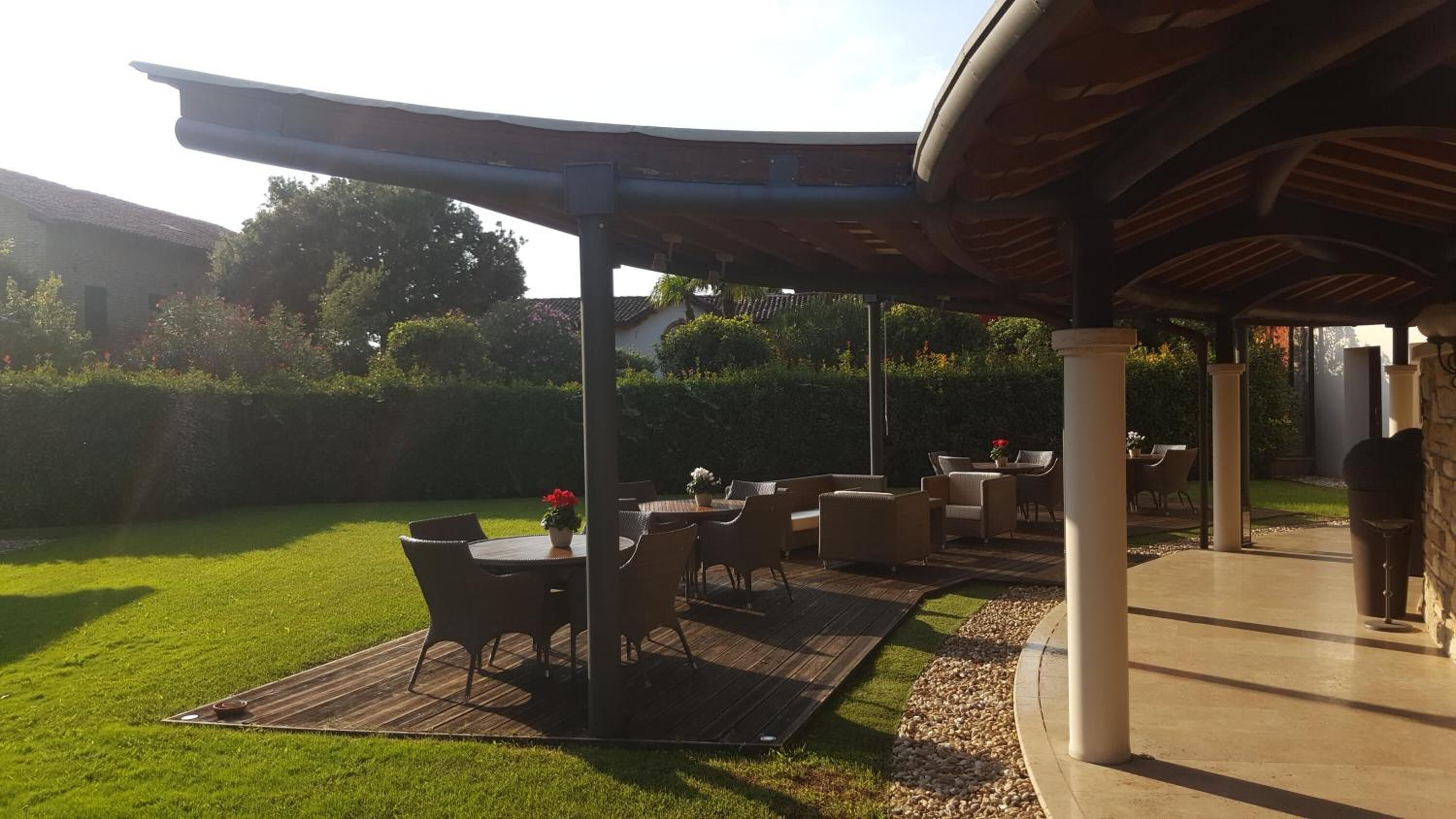 An outdoor patio area with a covered seating arrangement, a grassy lawn, and a stone pathway.