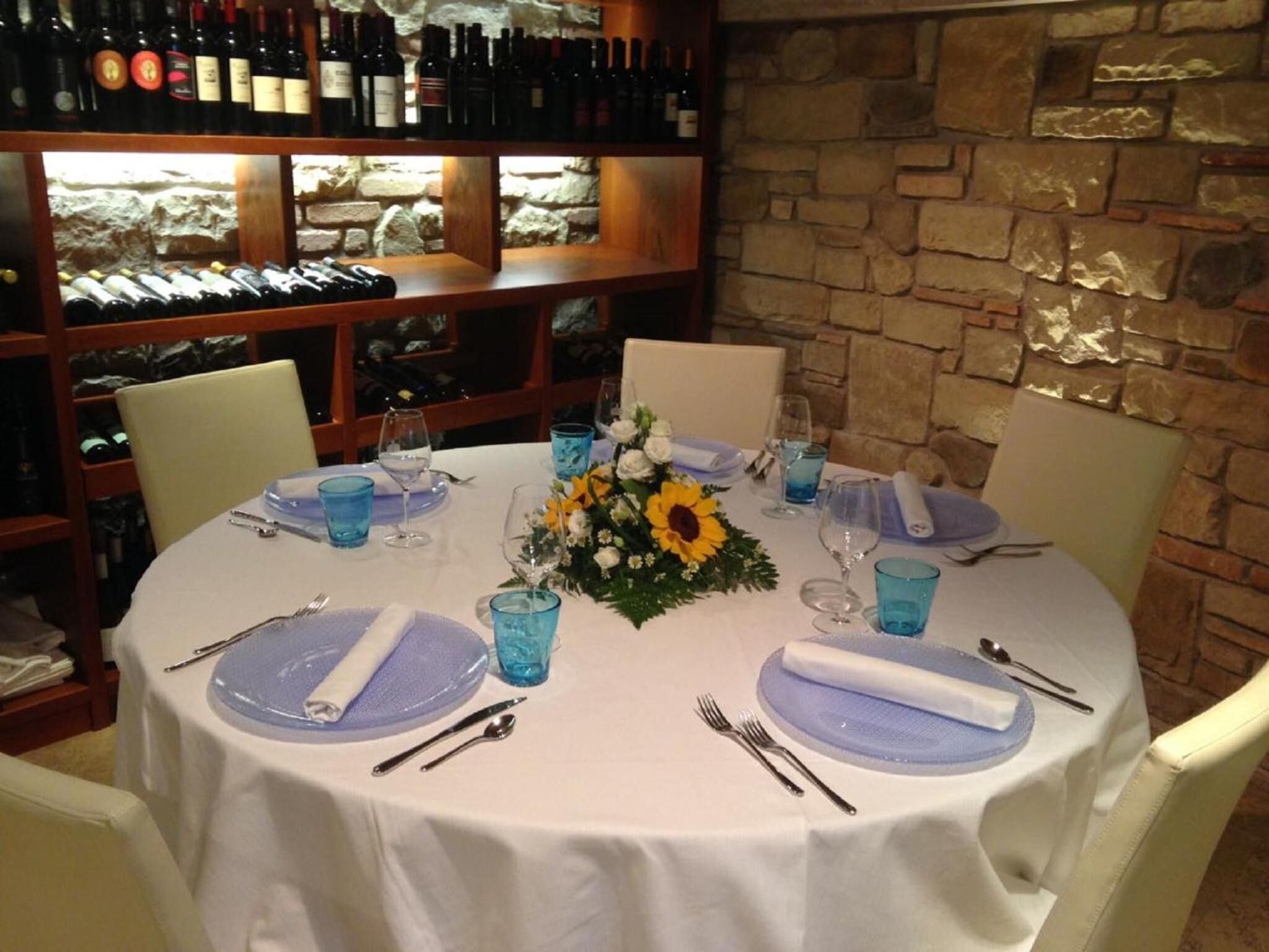 A round dining table set for four with white tablecloths, blue glassware, and a centerpiece of sunflowers.