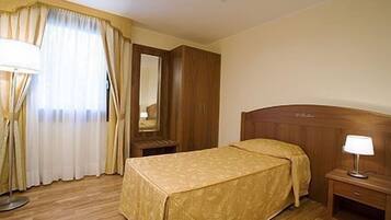 Una camera d'albergo con un letto di legno, un comodino con una lampada, uno specchio e una finestra con tende.