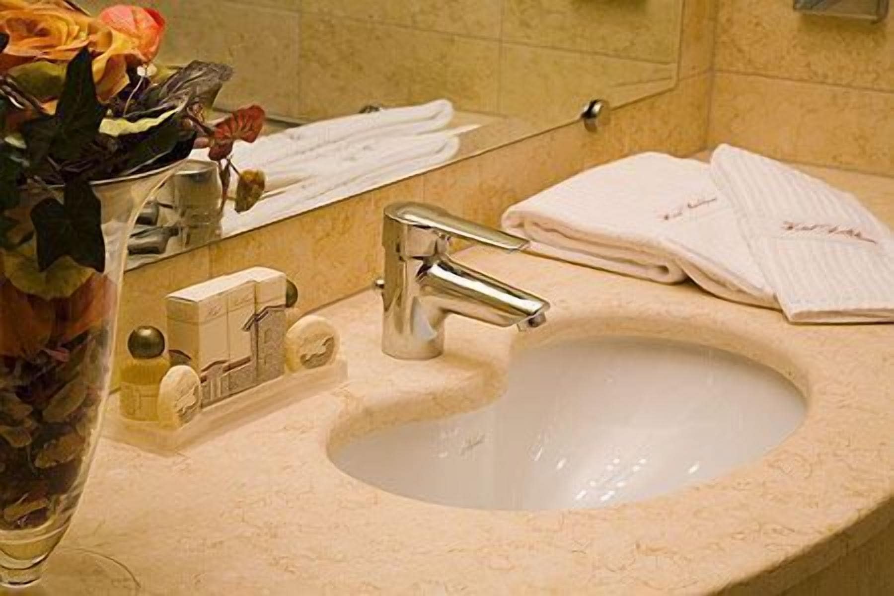 A bathroom sink with a mirror, a vase with flowers, and neatly folded towels.