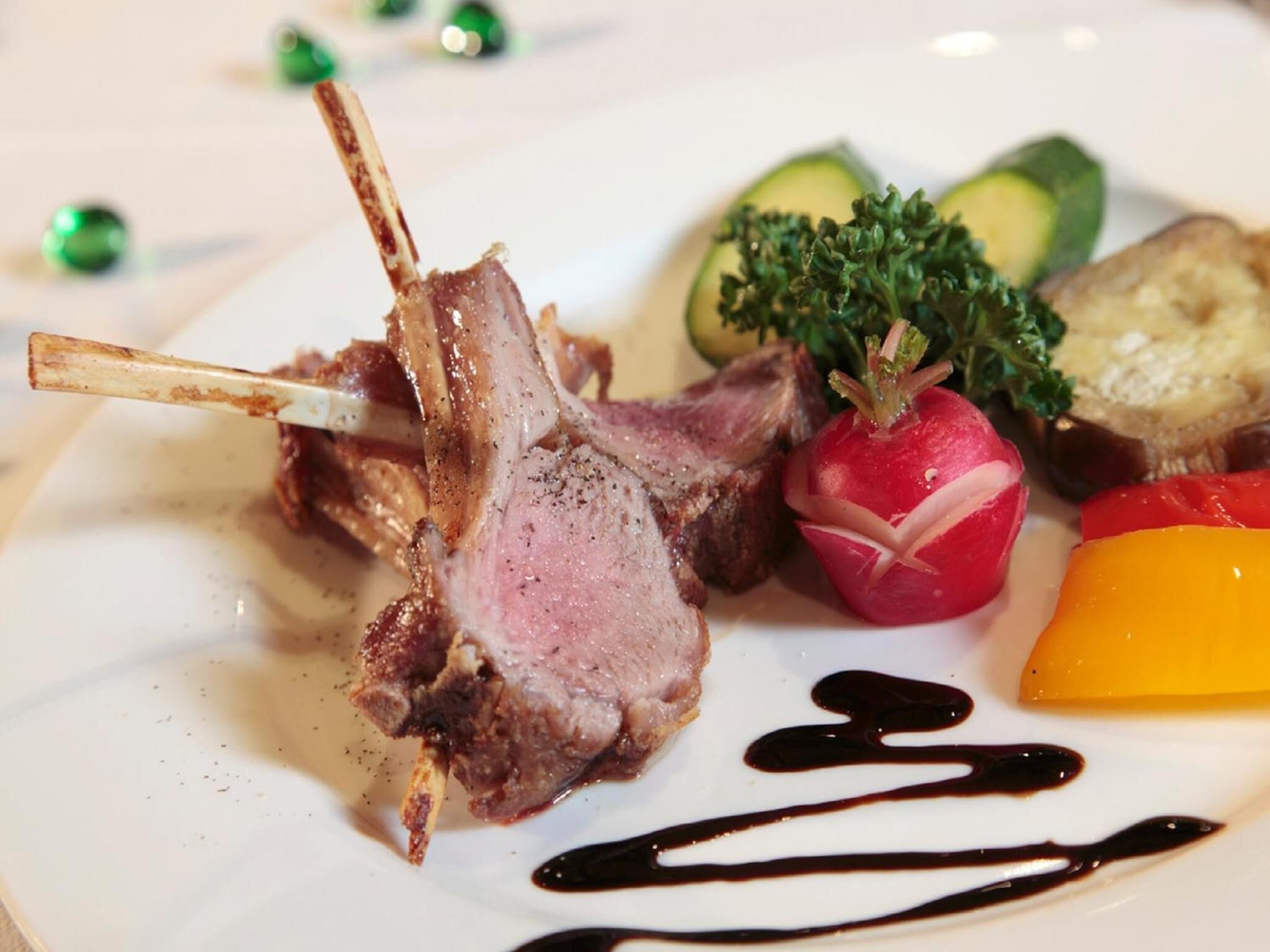 Un plato con un chuletón de cordero, verduras y salsa.