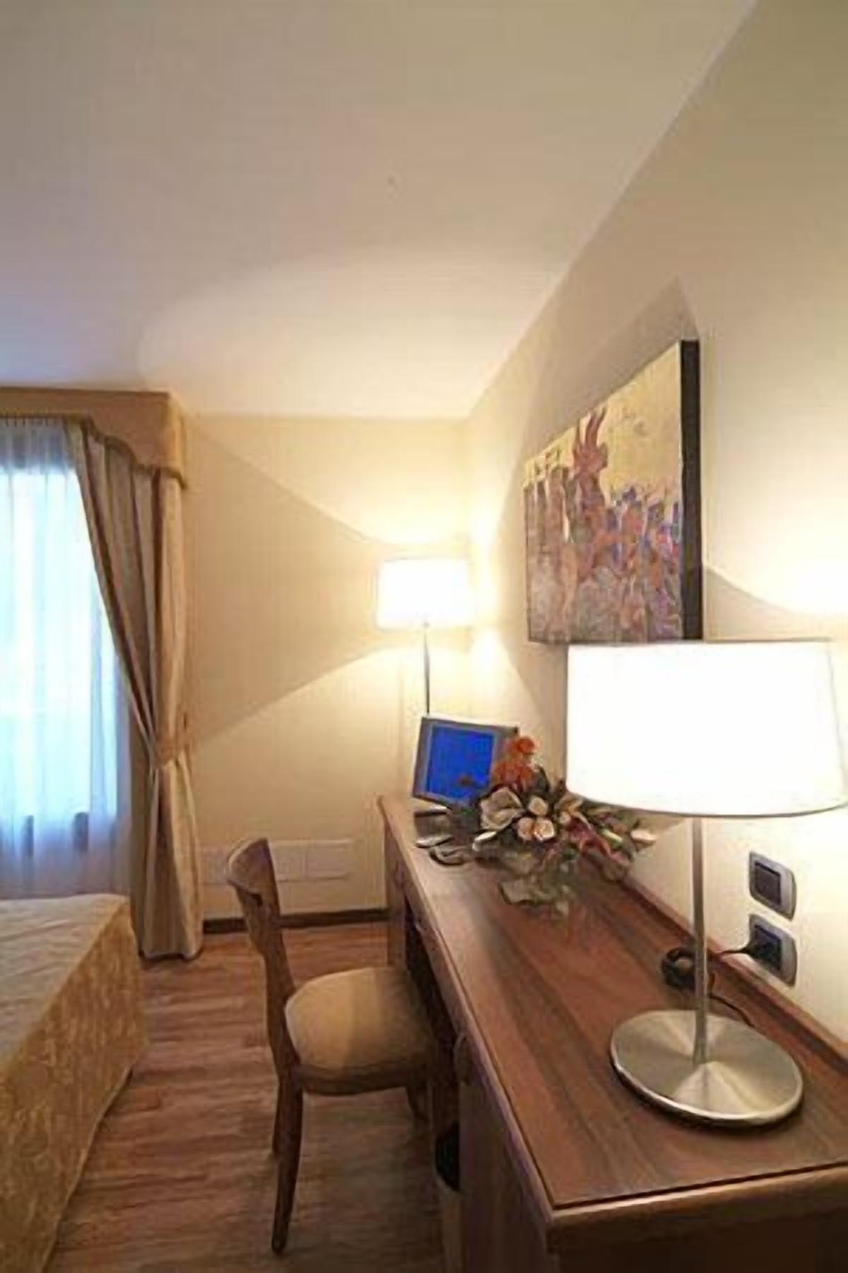 Ein Hotelzimmer mit einem Bett, einem Schreibtisch mit Computer, einem Sessel und einem Bild an der Wand.