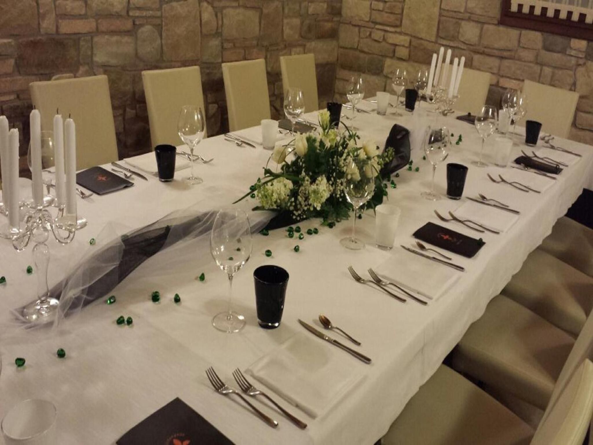 Una larga mesa de comedor dispuesta para un evento formal, con manteles blancos, velas y un centro de mesa floral.