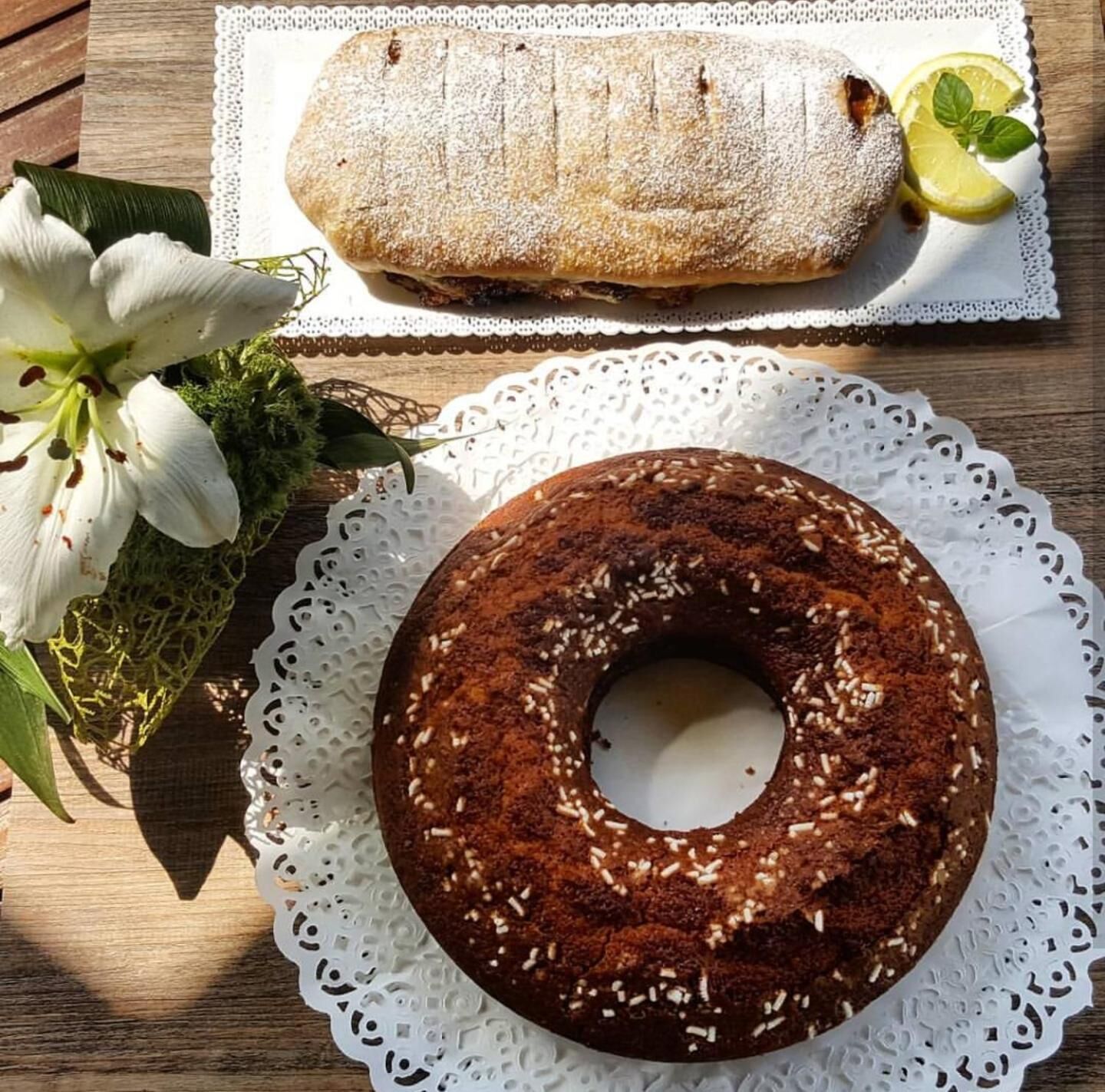 A loaf of bread and a cake on a wooden table with a lace doily.