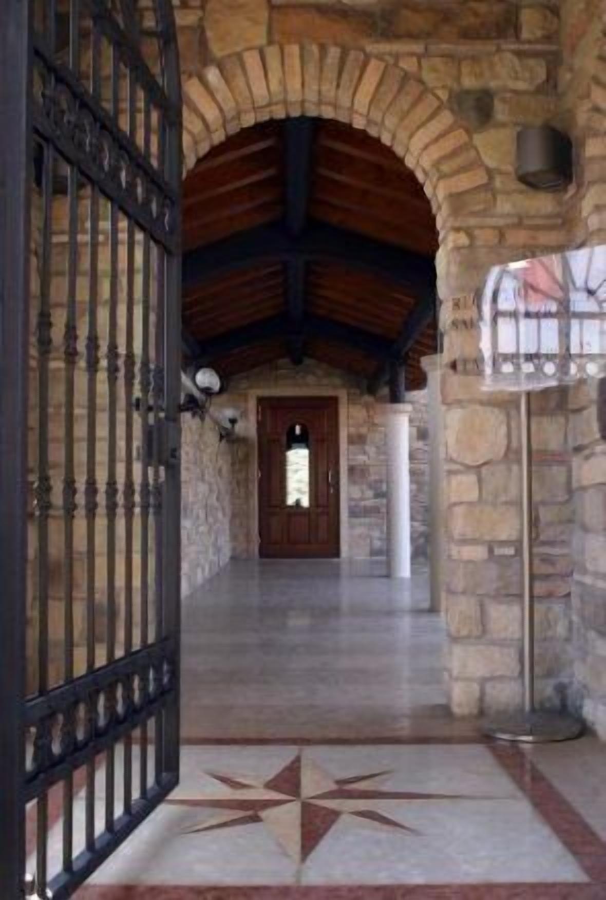 Un arc de pedra que dona a una porta de fusta, una reixa de metall i un paviment de rajoles amb un disseny d'estels.