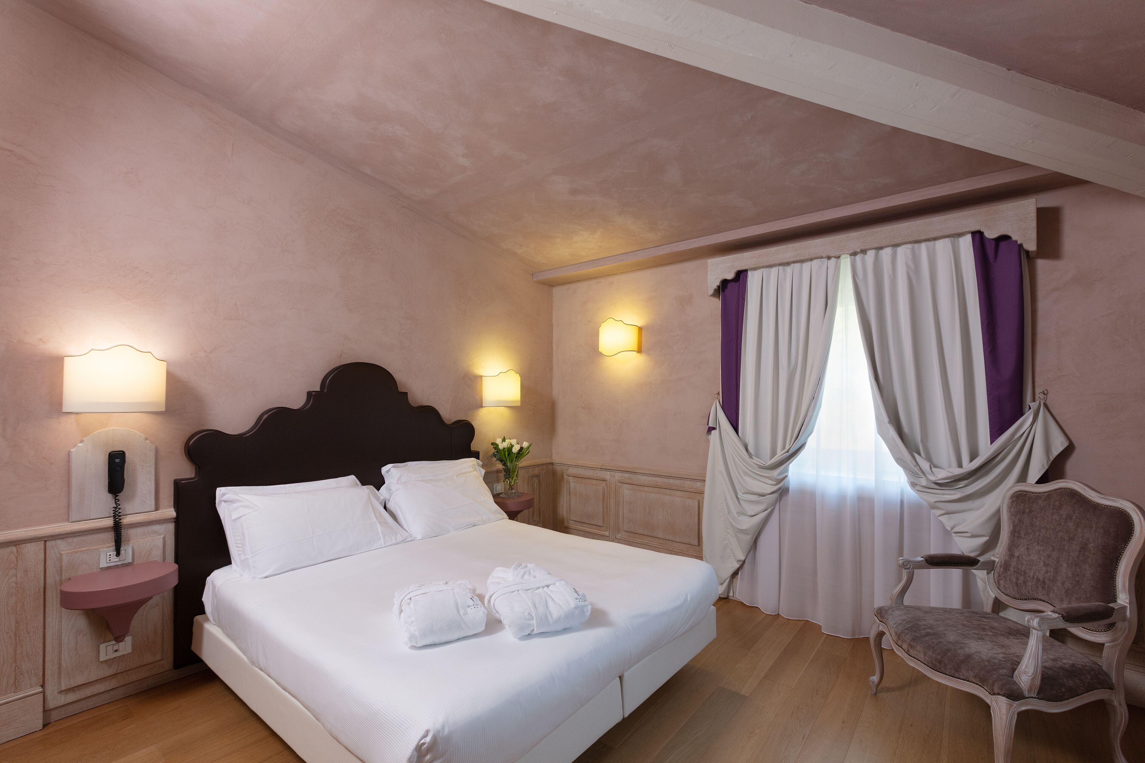 A hotel room with a large bed, bedside lamps, a vanity with a mirror, and a chair.