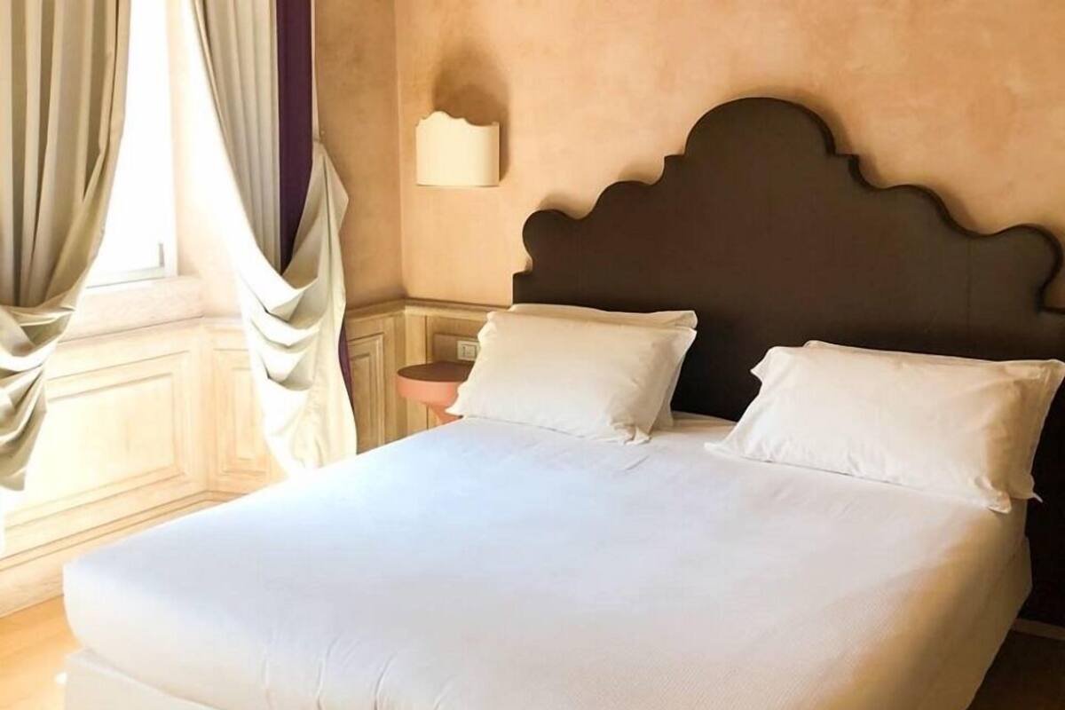 A large bed with white linens in a room with wooden flooring and a dark headboard.