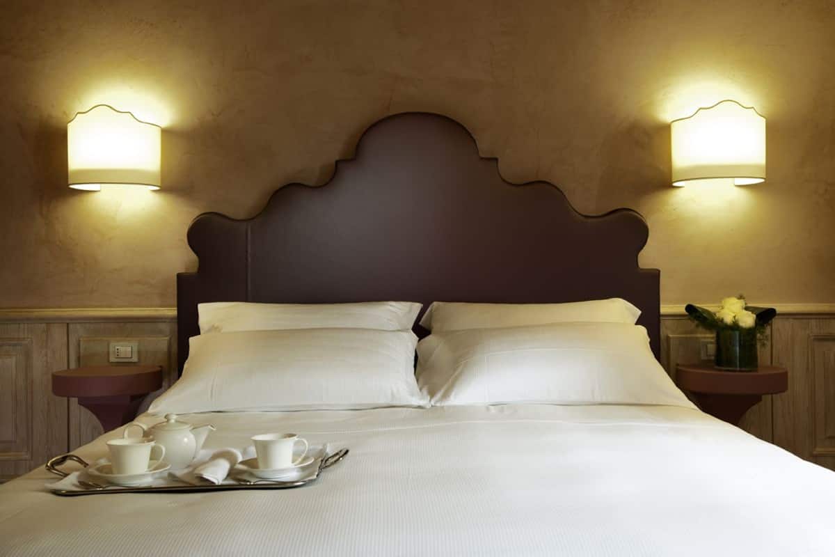 A neatly made bed with a tray of breakfast items, two bedside tables with lamps, and a decorative wall panel.