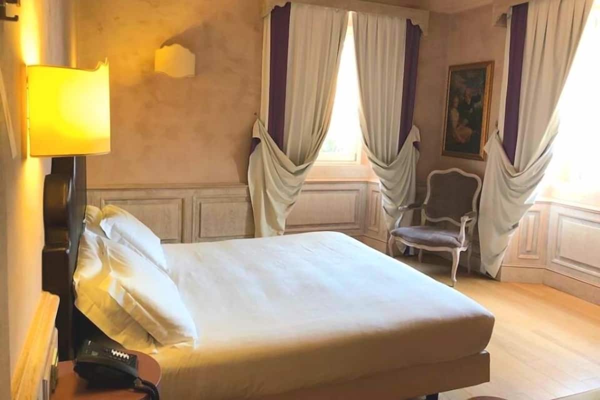 A hotel room with a bed, a chair, a lamp, and a painting on the wall.