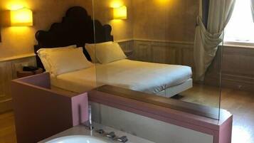Una camera d'hotel con un letto, lampade sui comodini, uno specchio grande, una vasca da bagno e una finestra con tende.