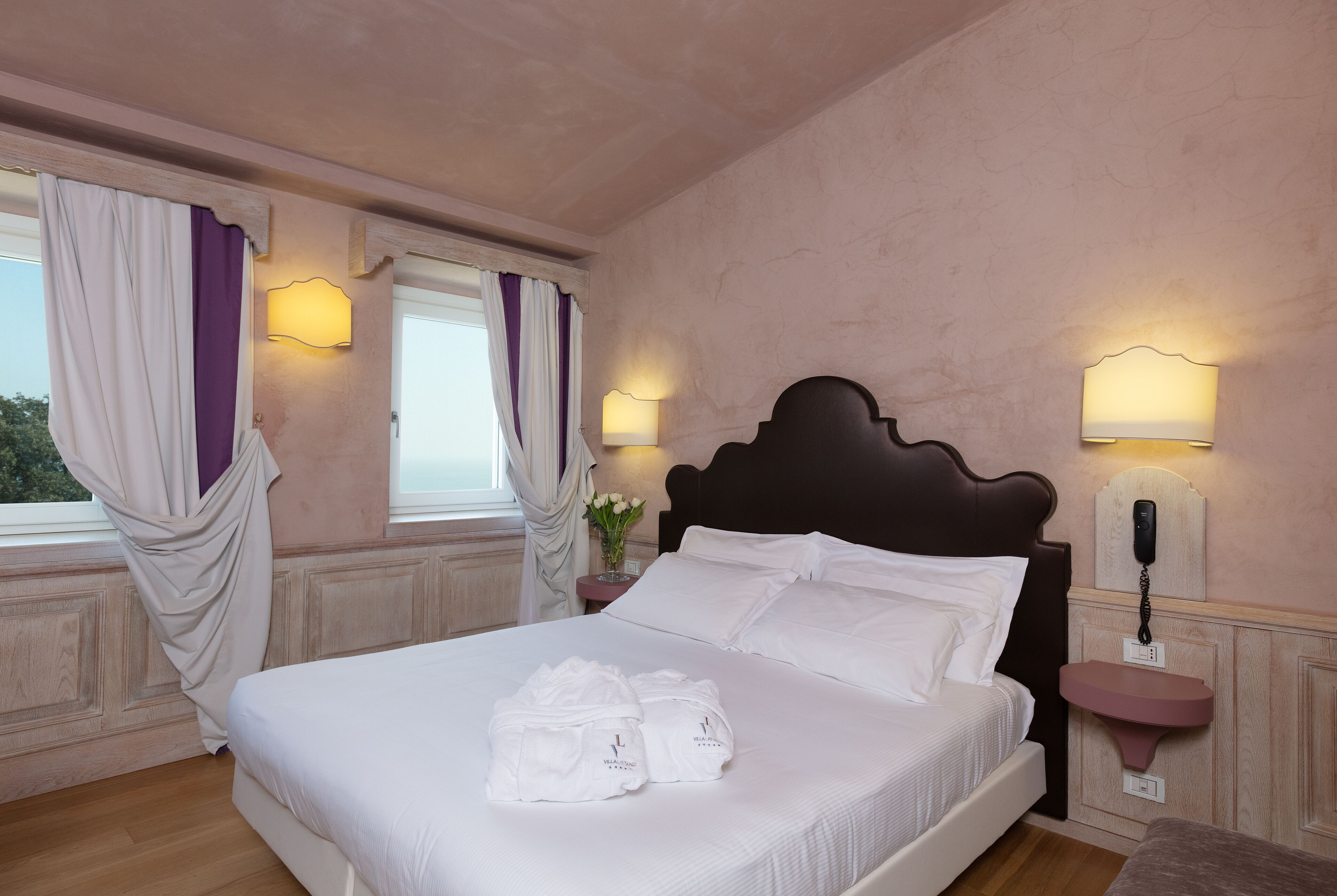 Un lit bien fait, avec du linge de lit et des serviettes blanches, une table de chevet avec une lampe et un téléphone fixé au mur.