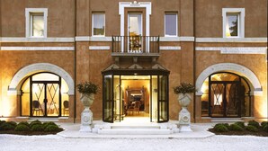 L’entrée d’un hôtel avec une façade en verre, un balcon et deux grandes portes en arc de cercle.