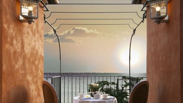 Un balcon avec une table et des chaises, une vue sur la mer et un coucher de soleil.