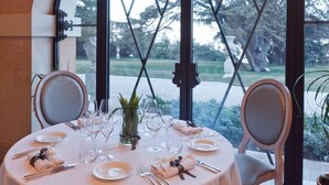 Une table ronde dressée pour le dîner, avec vue sur un jardin grâce à de grandes fenêtres.