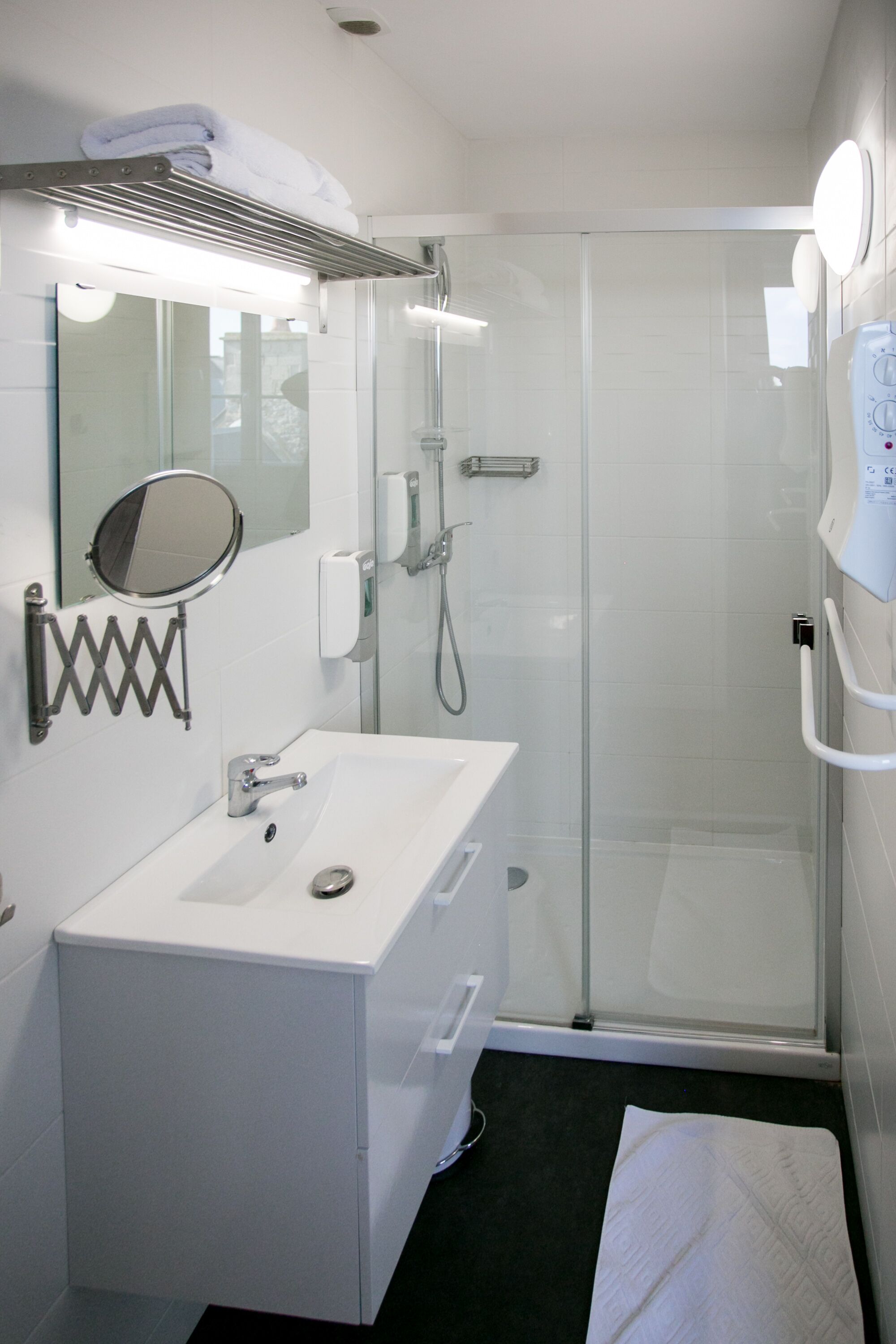 A modern bathroom with a glass shower enclosure, a white sink with a mirror, and a towel rack.