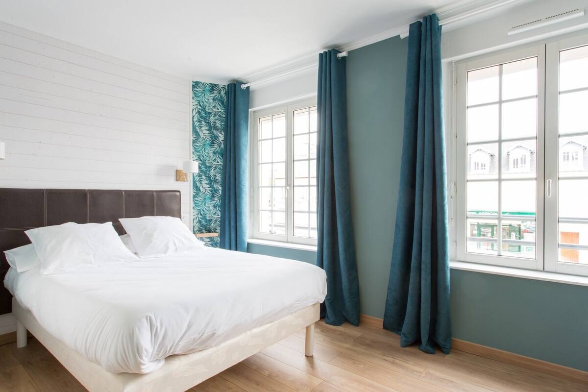 Een slaapkamer met een bed, een raam met gordijnen en een uitzicht op gebouwen.