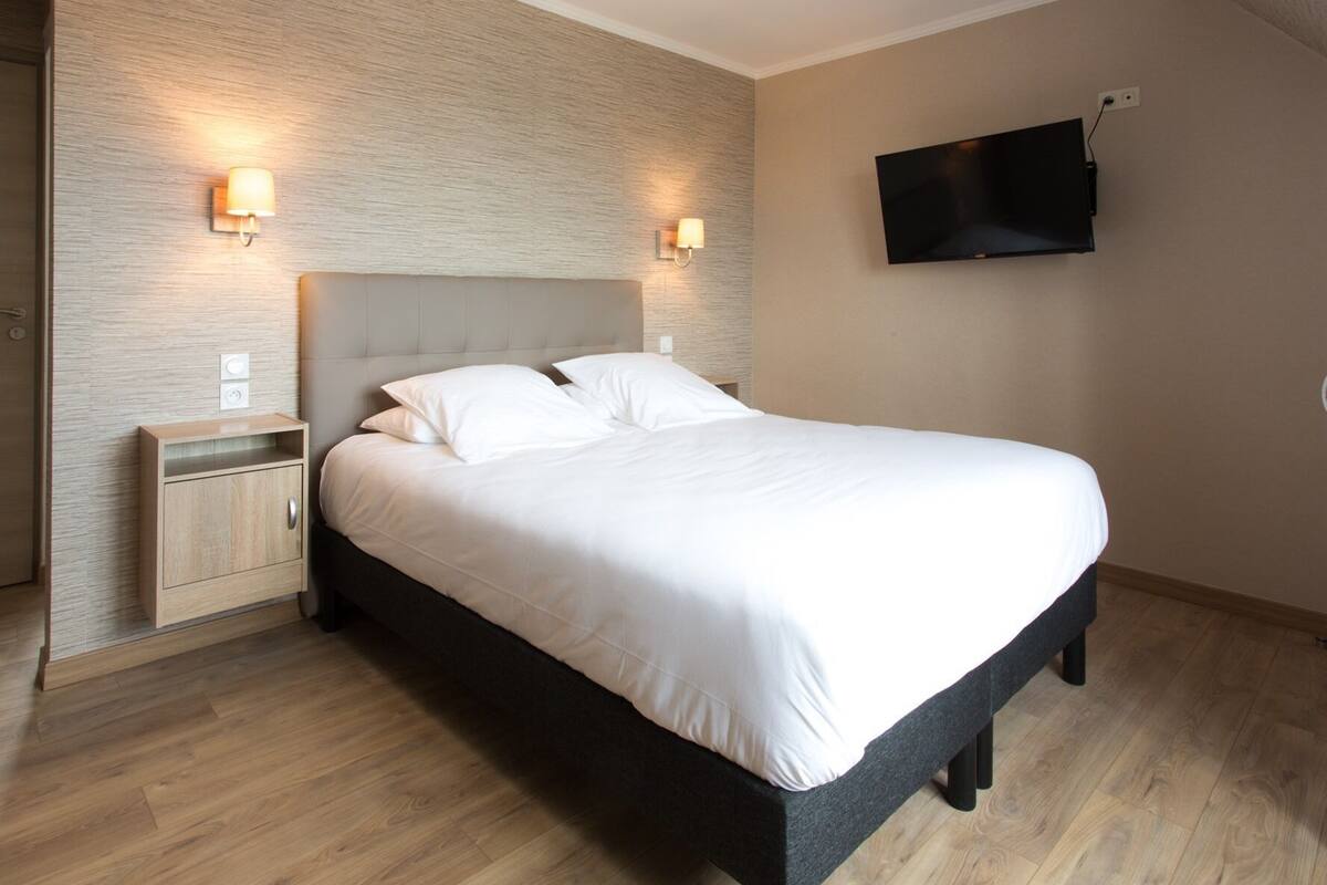 Een moderne hotelkamer met een groot bed, houten nachtkastjes, een flatscreen televisie aan de muur en een inbouwplank.