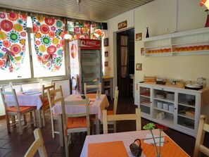 A dining area with wooden chairs and tables, a Coca-Cola refrigerator, and colorful window decorations. - Hostel Pisa Tower (Pisa)