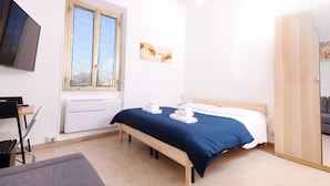 Ein Schlafzimmer mit Bett, Schreibtisch, Stuhl, Fernseher und Fenster.