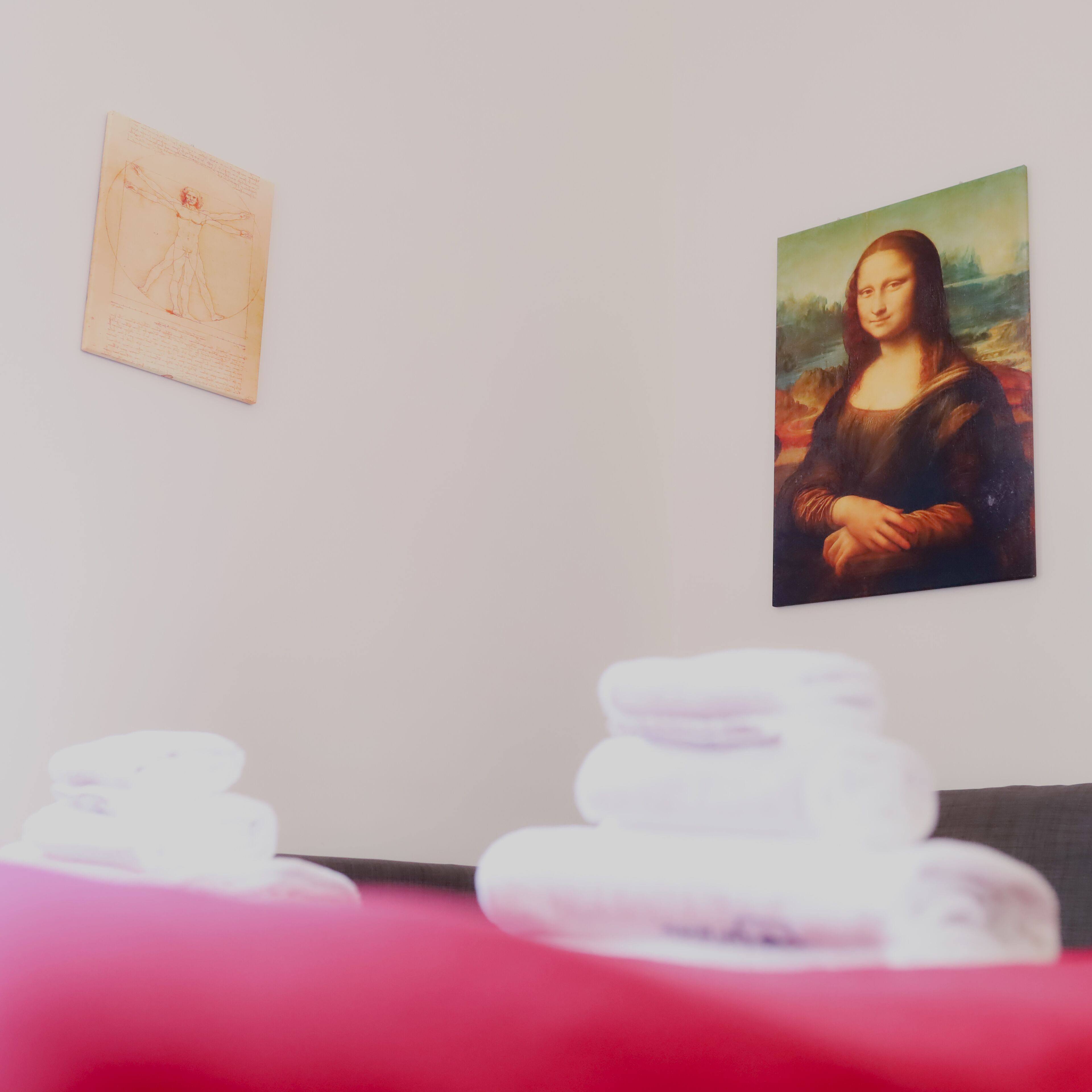 A room with a painting of the Mona Lisa on the wall, a sketch on the left, and a stack of white pillows in the foreground.