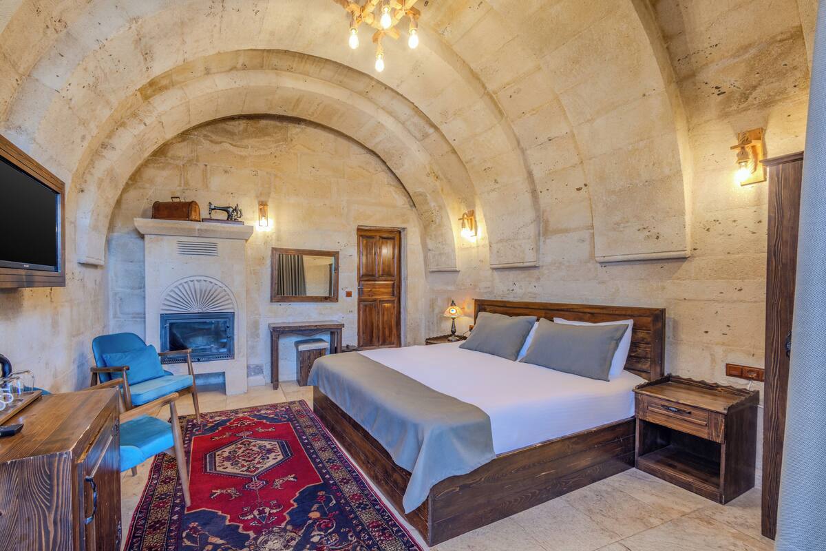 A bedroom with a large bed, a fireplace, a wooden desk, and a television.