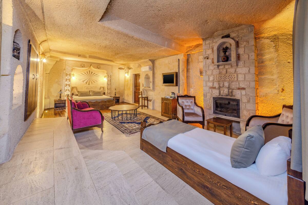 A cozy room with a bed, a sofa, a small table, and a fireplace.