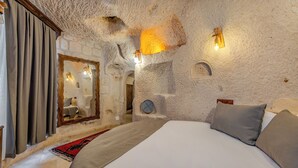 Un dormitorio con pared de piedra, una cama con almohadas, un espejo y una lámpara.