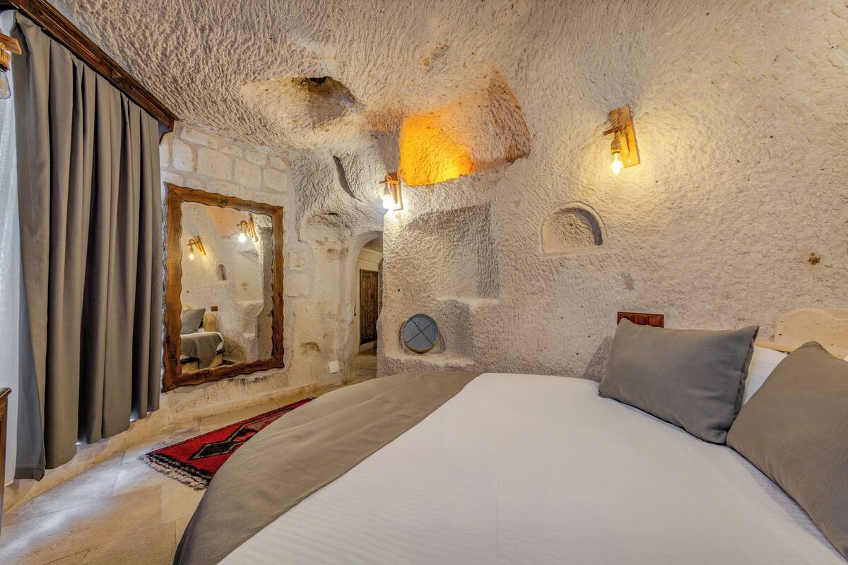 A bedroom with a stone wall, a bed with pillows, a mirror, and a light fixture.