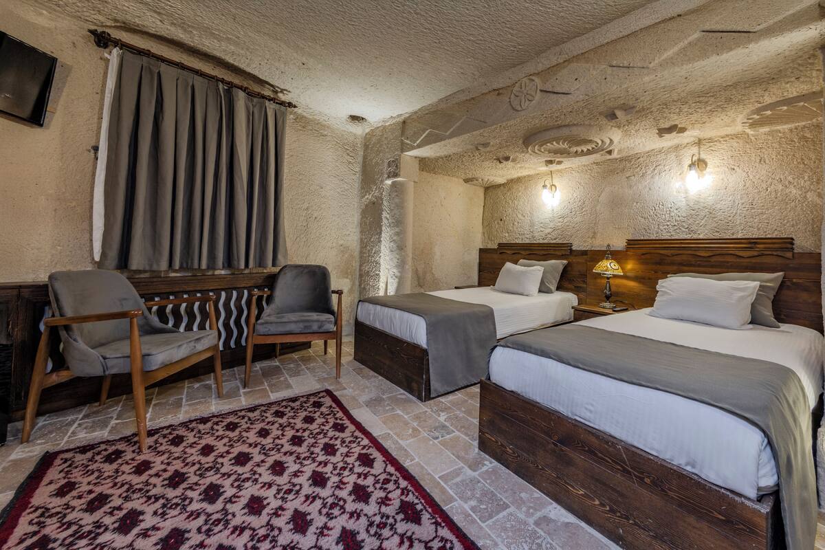 A room with two beds, a wooden chair, a small table, and a patterned rug.