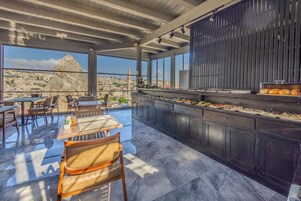 Un área de comedor en la azotea con una barra larga, asientos y vistas a un paisaje urbano.
