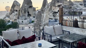 Una terraza en la azotea con mobiliario exterior, vistas a formaciones rocosas y globos aerostáticos al fondo.
