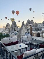 A rooftop terrace with outdoor seating, a view of rock formations, and hot air balloons in the background.