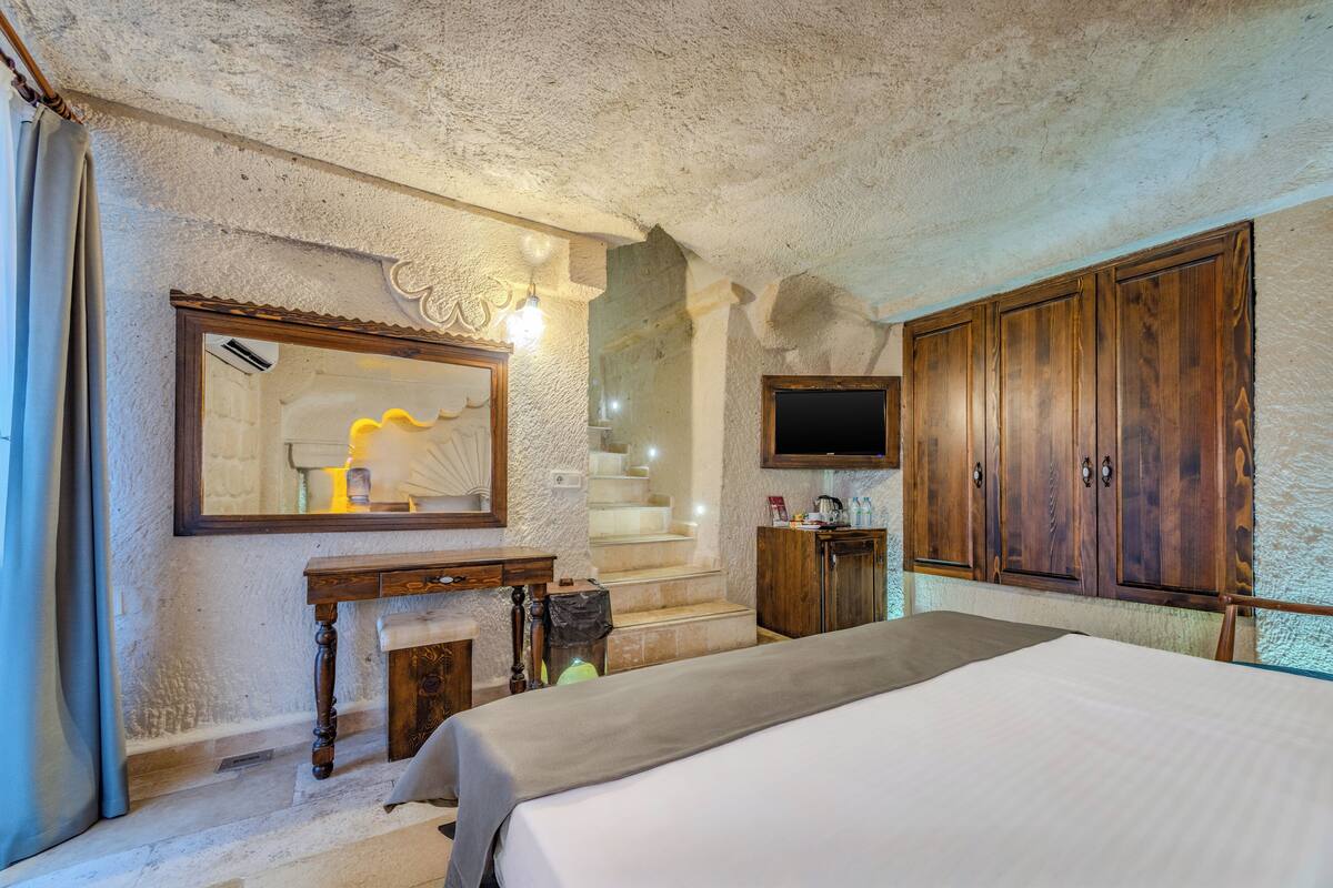 A bedroom with a bed, a wooden wardrobe, a television, and a mirror.