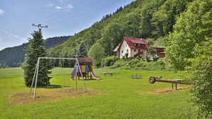 A playground with swings and a slide, a picnic table, and a bench in a grassy field with a house in the background. - Grüner Hof (Zell am Harmersbach)