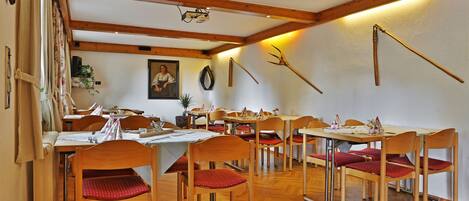 Un espace repas avec des tables et des chaises en bois, un plafond avec des poutres apparentes et un miroir fixé au mur.