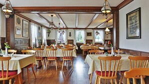A spacious dining hall with wooden tables and chairs, large windows, and hanging light fixtures. - Grüner Hof (Zell am Harmersbach)