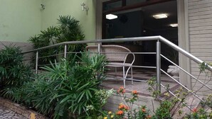 Entrada de un edificio con una escalera de metal, un banco de mimbre y plantas en macetas.