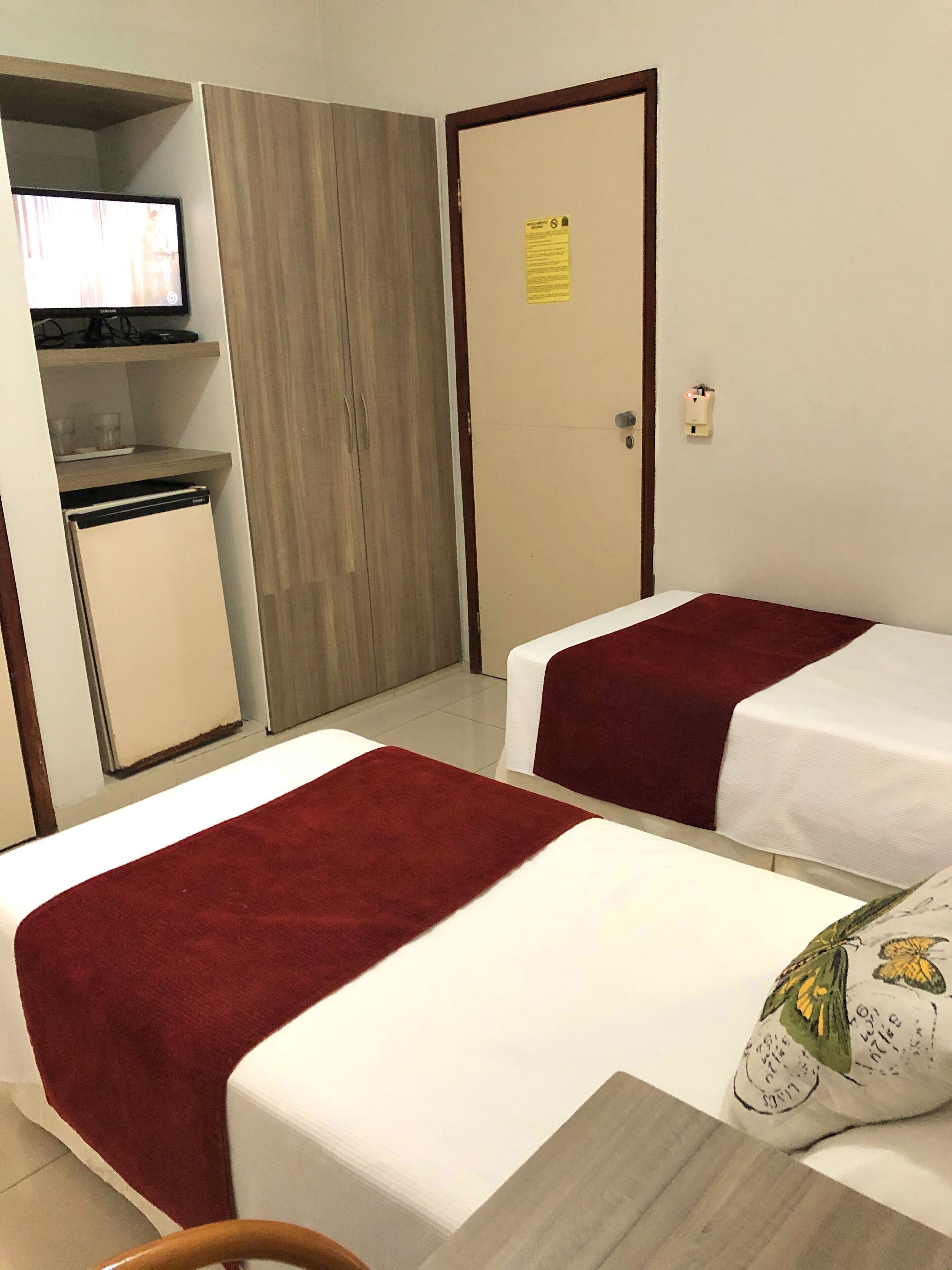 A hotel room with two beds, a small kitchenette, a television, and a door with a notice.