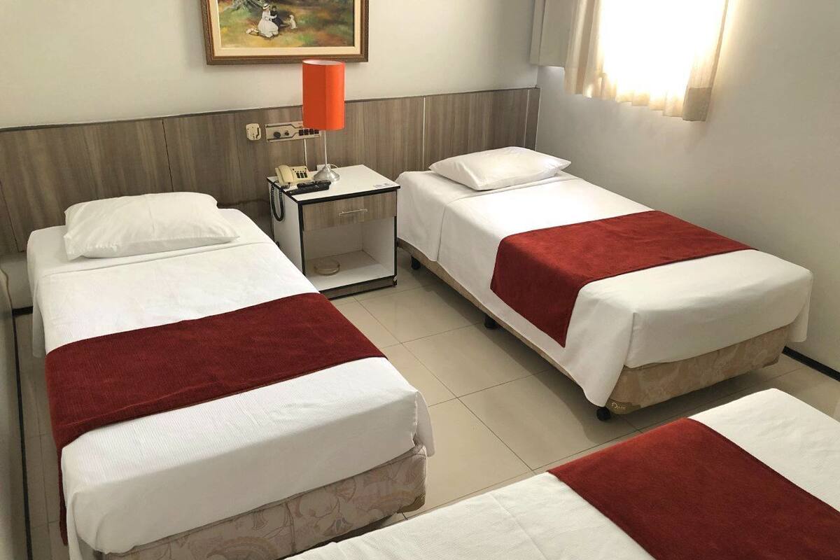 A hotel room with two single beds, a nightstand with a lamp, and a painting on the wall.